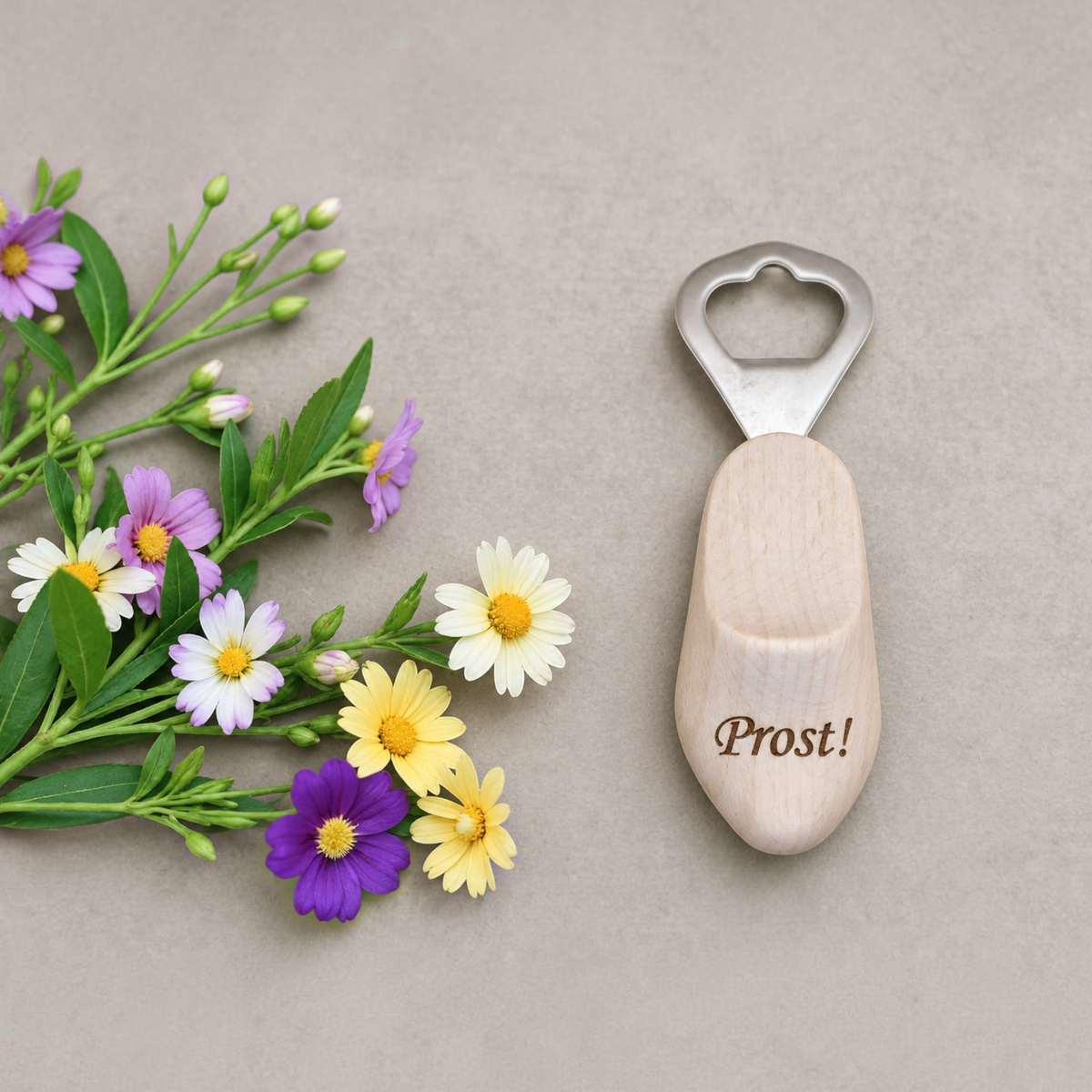 HUNTERLASE Flaschenöffner aus hellem Holz in Holzschuh-Form mit Prost-Gravur neben bunten Wiesenblumen